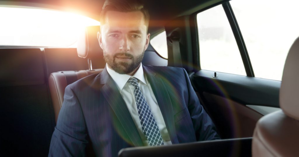 Serious businessman with laptop sitting in a comfortable car